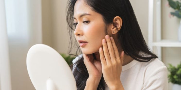 Woman looking at her dull skin in the mirror